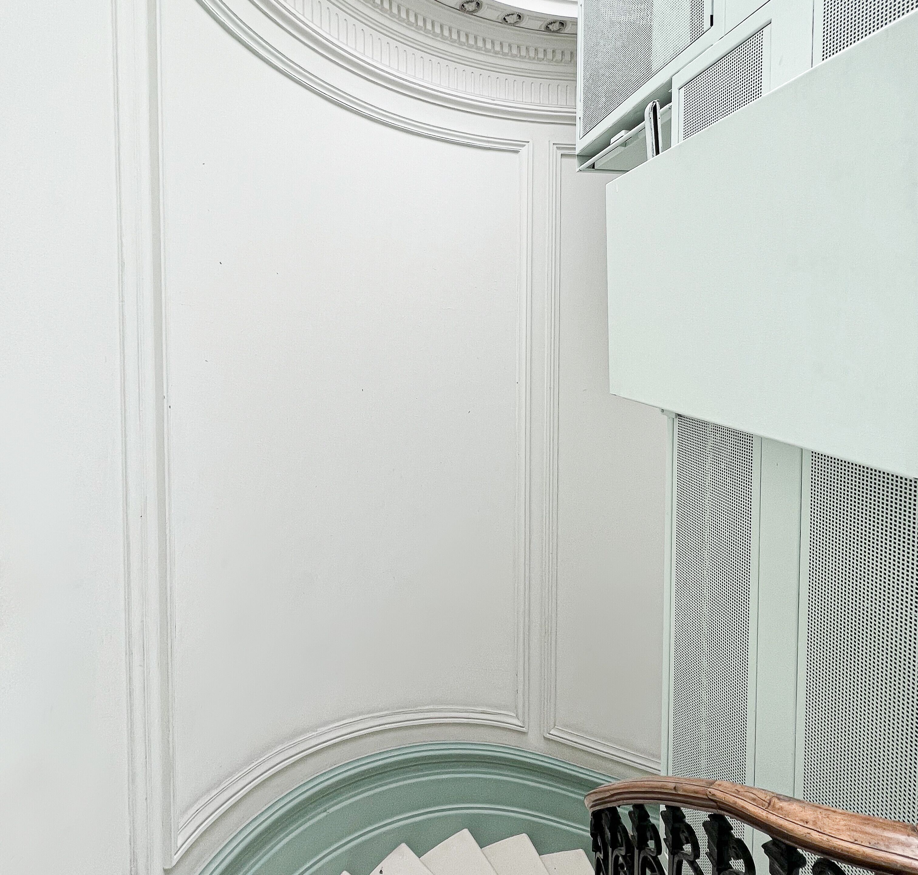 Una escalera con barandilla de madera y pared blanca con molduras decorativas.