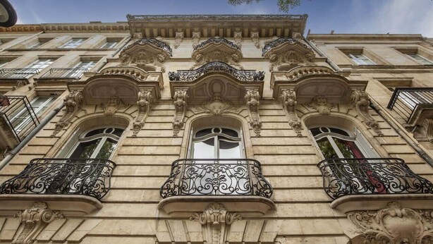 Une façade d’immeuble ornée de détails architecturaux raffinés, notamment des balcons décoratifs et des fenêtres au style classique.
