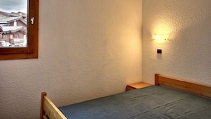 Et lille, enkelt møbleret værelse med en seng, et lille bord og et vindue med udsigt til huse.
