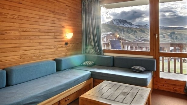 Et træinteriør med en sofa og et bord, et vindue med udsigt til bjerge, og en gardin.