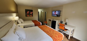 Una habitación de hotel con dos camas, un escritorio, un televisor y un cuadro en la pared.