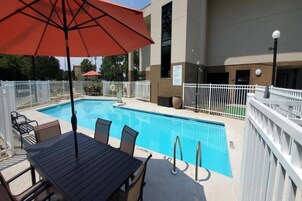 Una piscina con mesa y sillas, rodeada por una cerca blanca y un paraguas rojo.