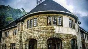 Un edificio de piedra con una esquina redondeada, ventanas grandes y una chimenea.