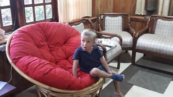 Un enfant est assis sur une chaise rouge dans une pièce dont le mobilier est en bois et dont le sol est recouvert de carreaux.