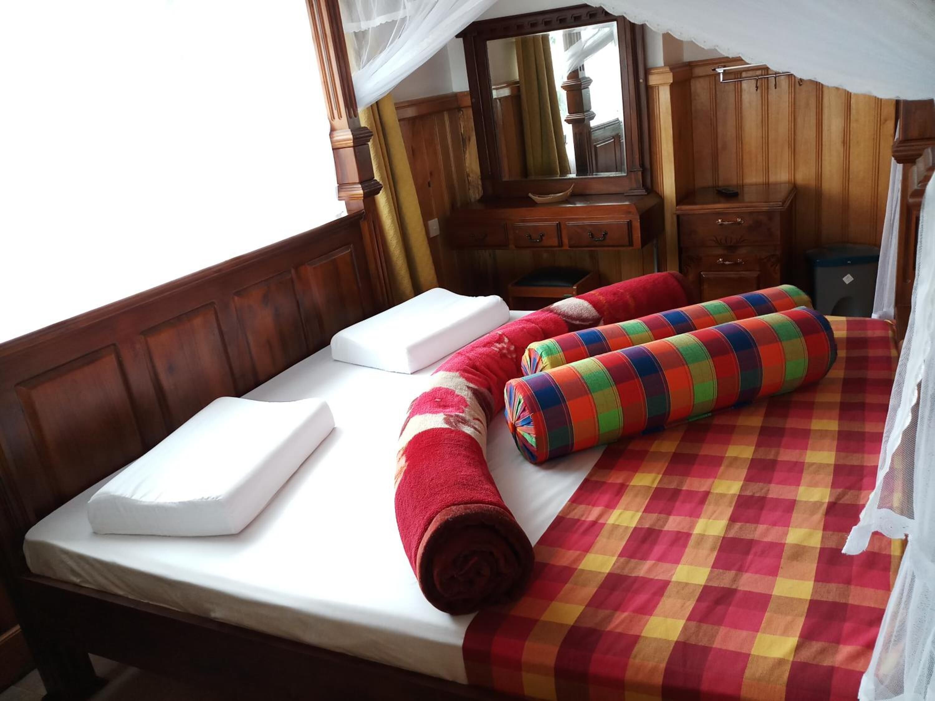 A bed with white linens, a colorful checkered bedspread, and rolled towels.