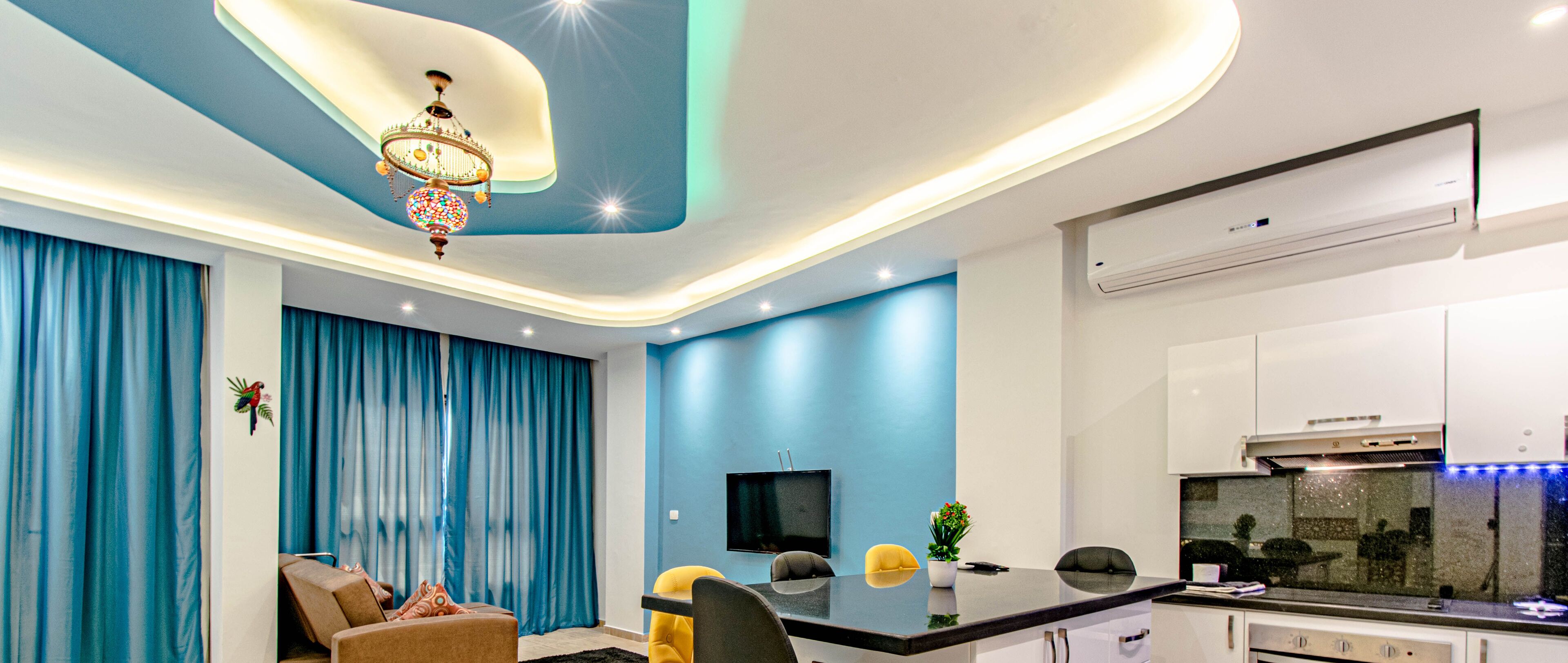 A modern living room with a dining area, a kitchen, and a TV mounted on the wall.