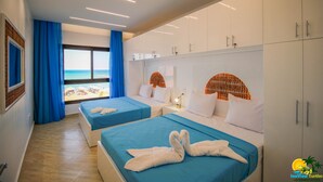 Habitación de hotel con dos camas, un ventanal amplio con vistas a la playa y un armario con varios compartimentos.