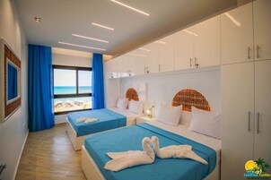 Habitación de hotel con dos camas, un ventanal amplio con vistas a la playa y un armario con varios compartimentos.