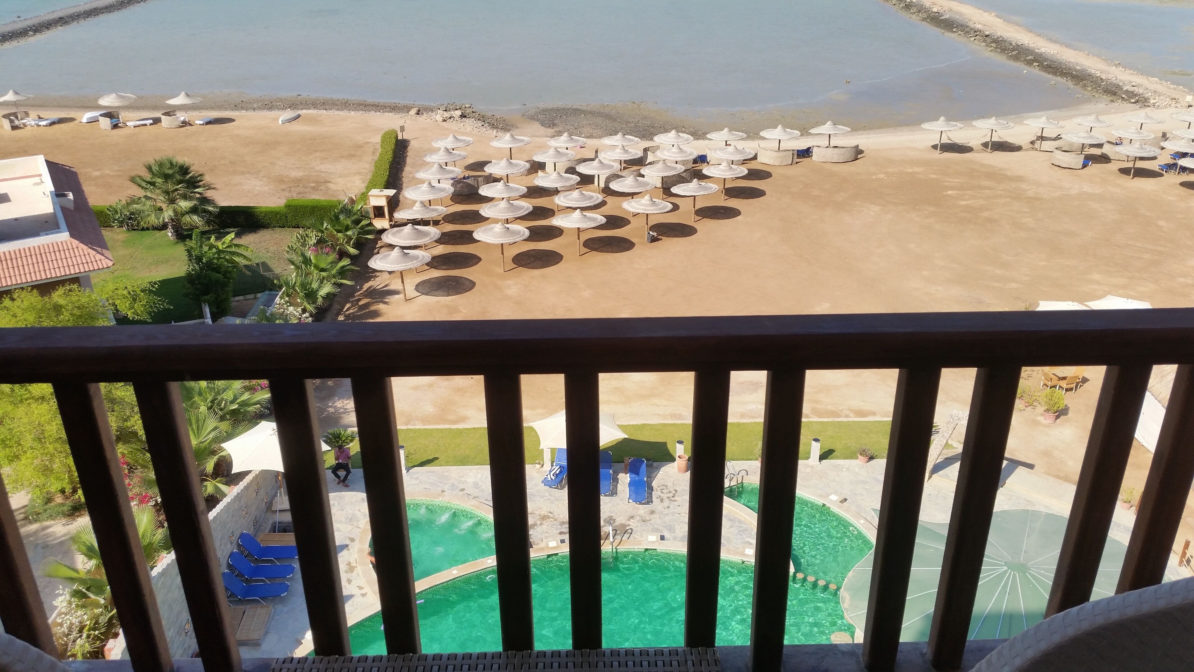 A beach with umbrellas and lounge chairs, a pool, and a view of the sea.