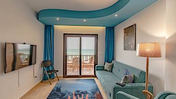 Una sala de estar con sofá, televisión, sillón, lámpara y vista a la playa a través de un ventanal.