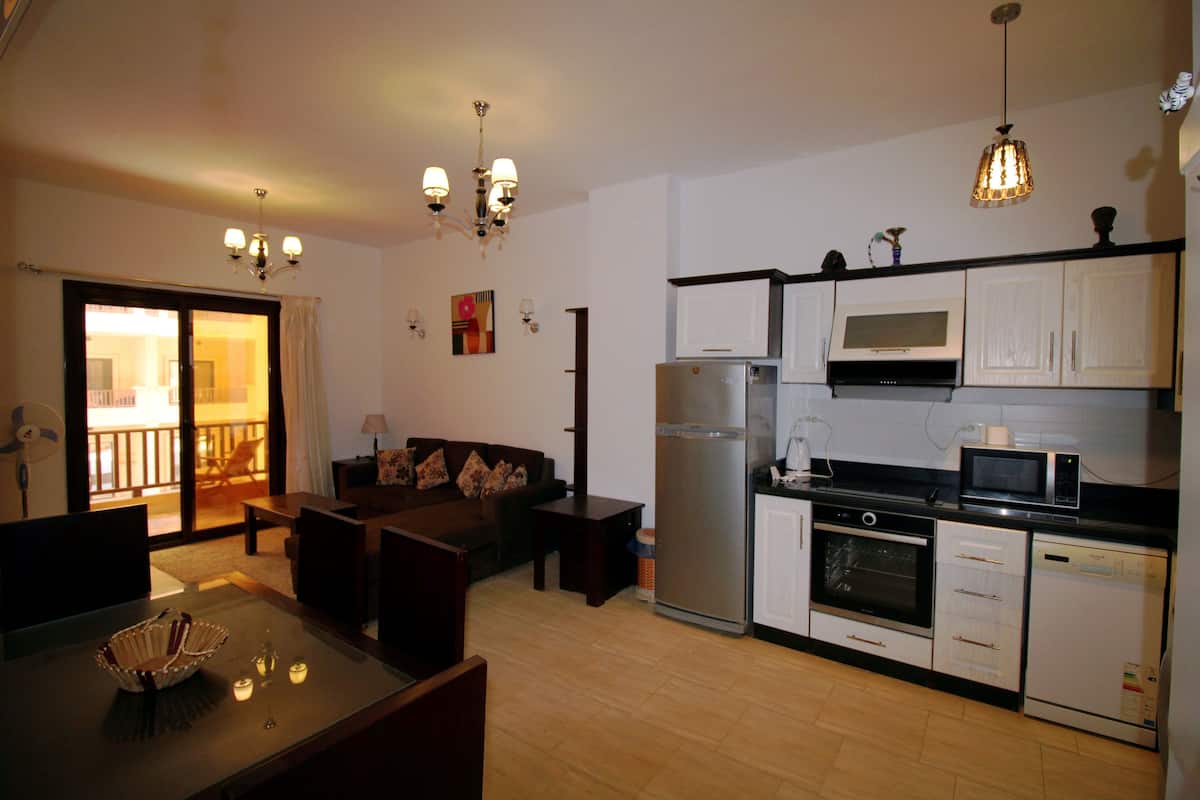 A compact kitchen with a refrigerator, microwave, oven, and dishwasher. There is a dining area with a table and chairs.