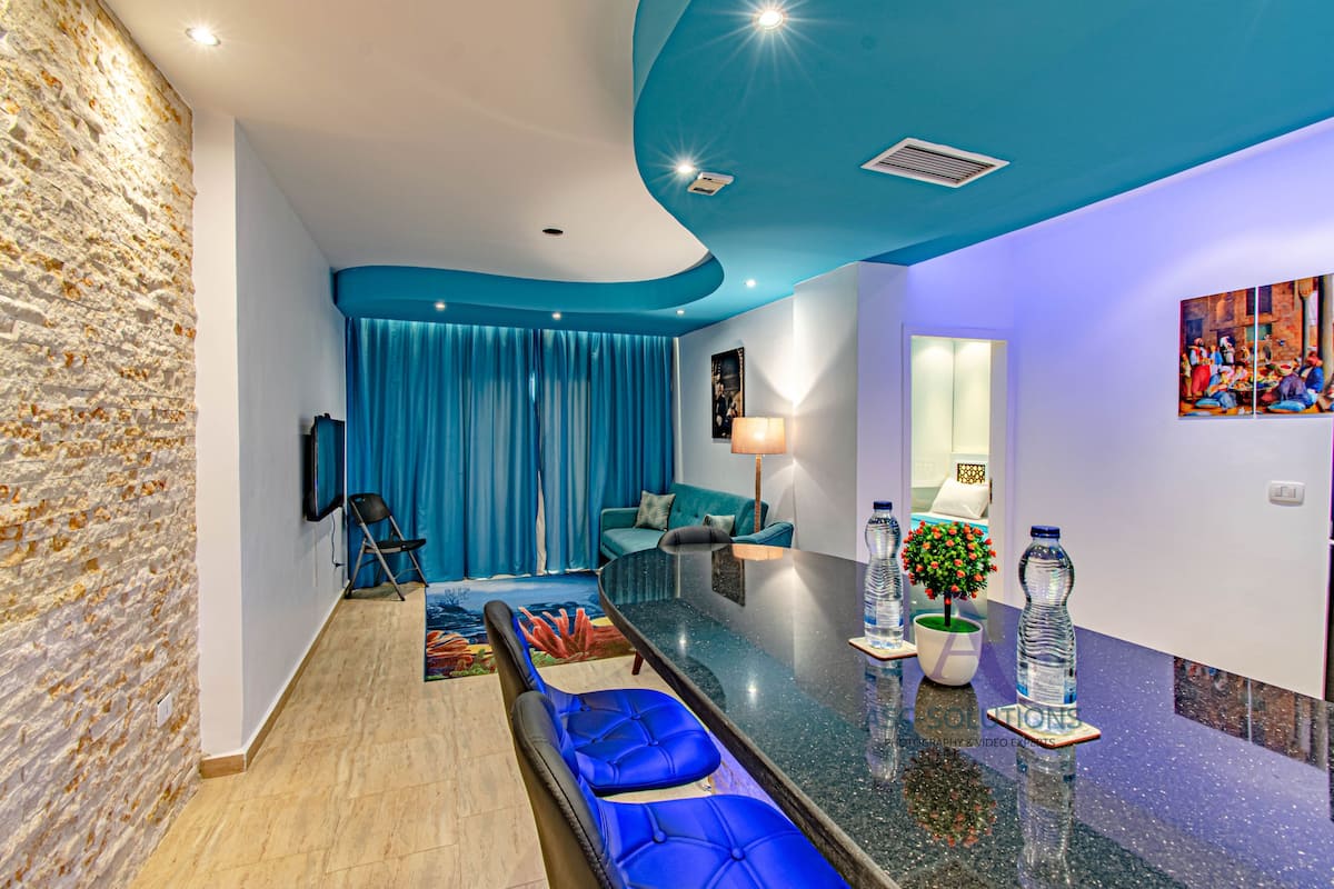 A modern living room with a stone wall, blue curtains, a teal sofa, a blue bar area, and a small plant.
