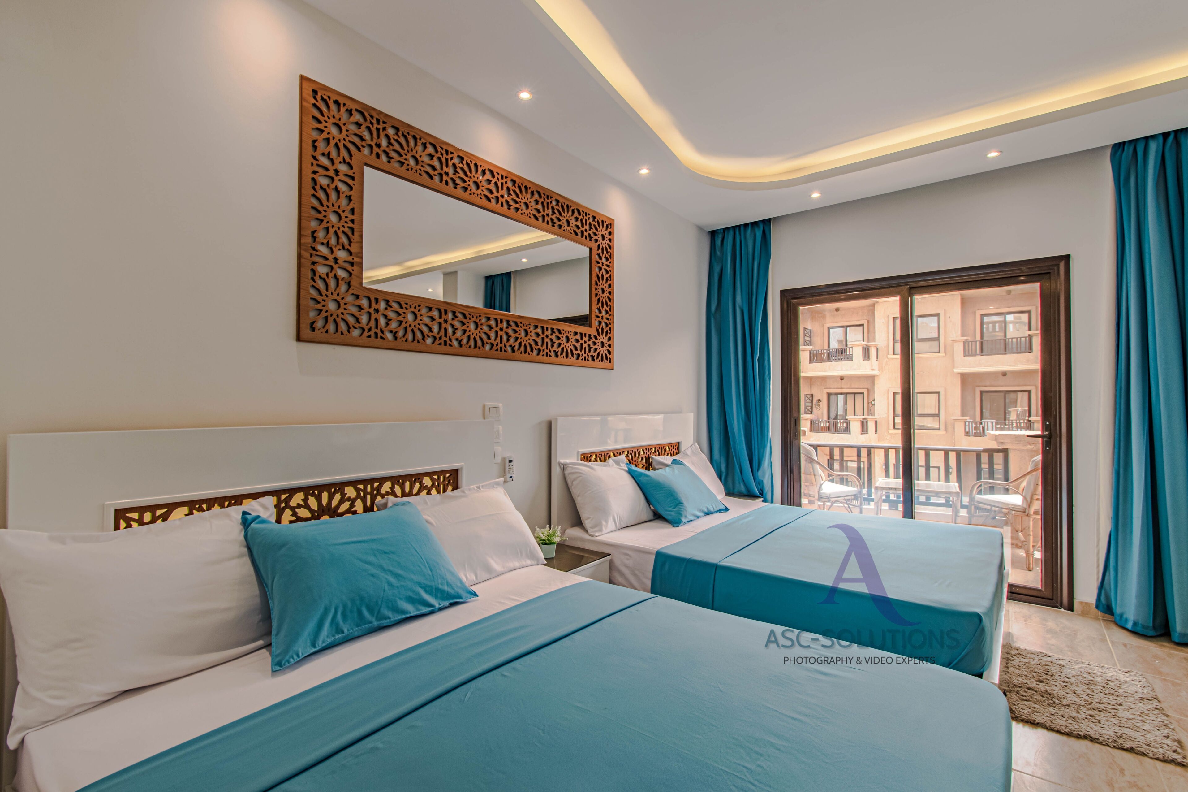 Une chambre d’hôtel avec deux lits, un grand miroir et un balcon avec des rideaux bleus.
