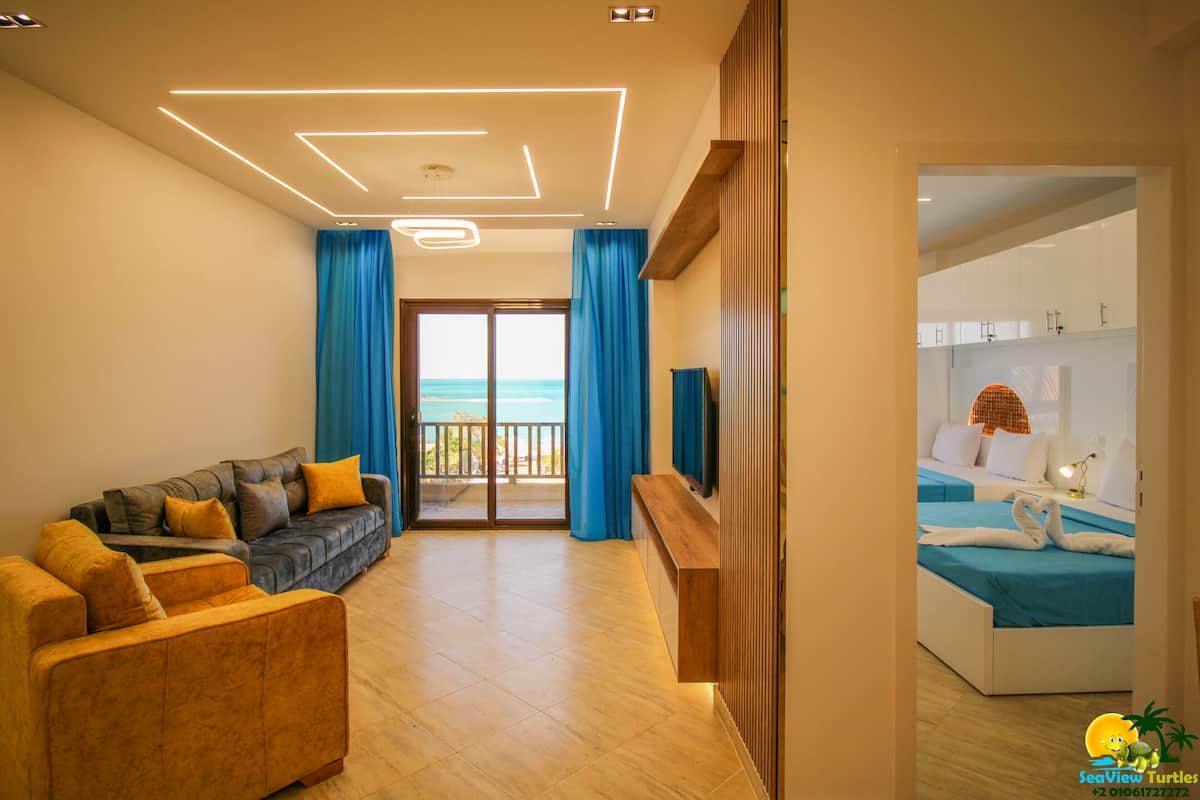 A modern living room with a sofa, a wooden TV stand, and a balcony with blue curtains.