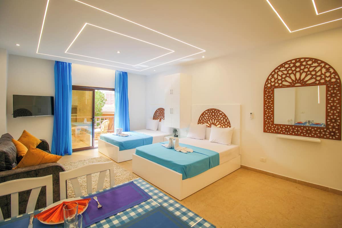 A modern hotel room with two beds, a TV, and a balcony with blue curtains.