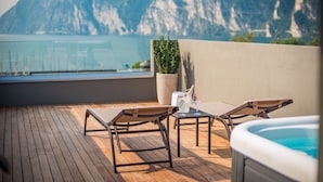 A wooden deck with lounge chairs and a hot tub, overlooking a body of water and mountains. - Hotel Villa Enrica (Riva del Garda)