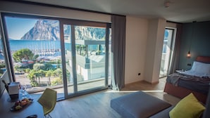 A modern hotel room with a large sliding glass door leading to a balcony with a view of the sea and boats. - Hotel Villa Enrica (Riva del Garda)