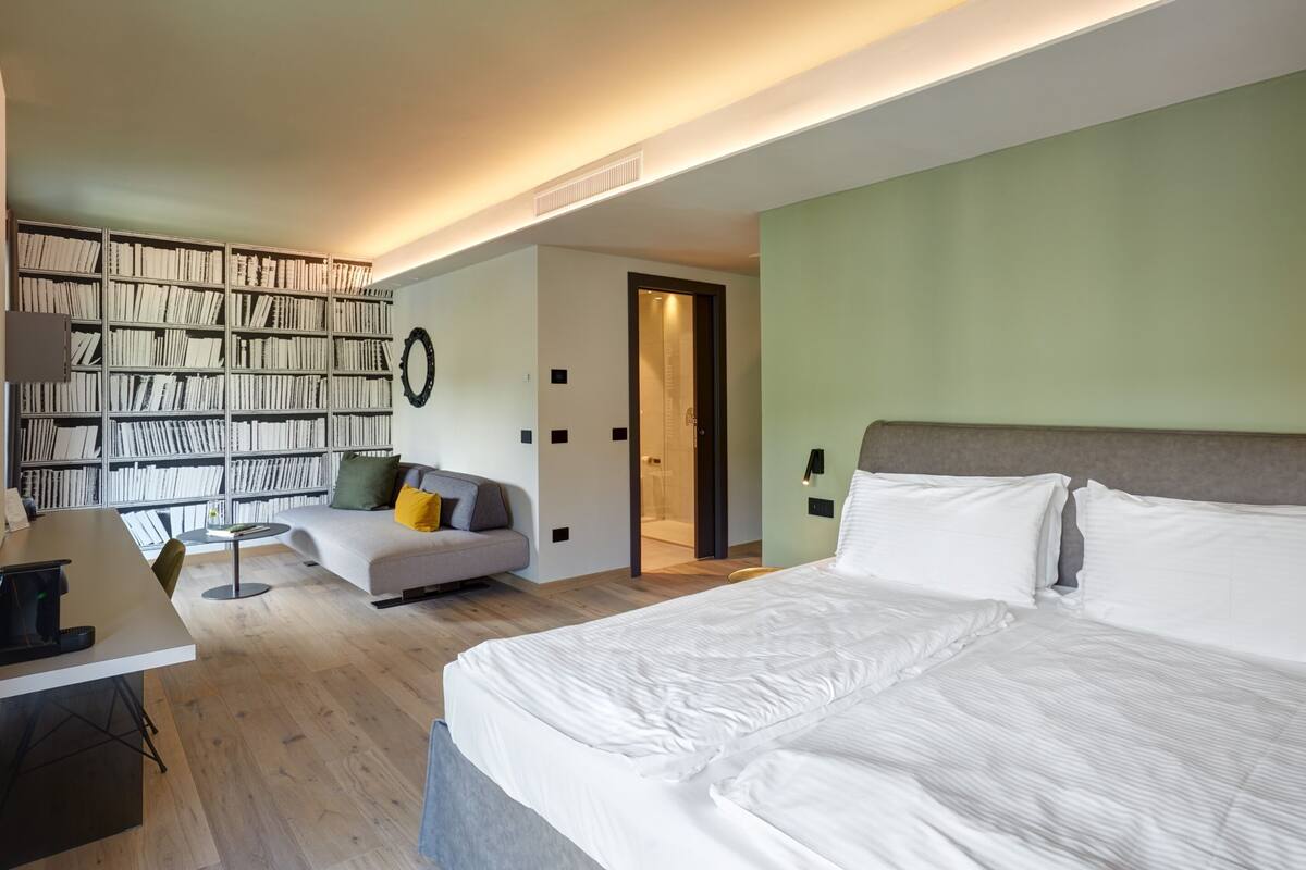 Un dormitorio moderno con una cama grande, un sofá, una mesita y una estantería.