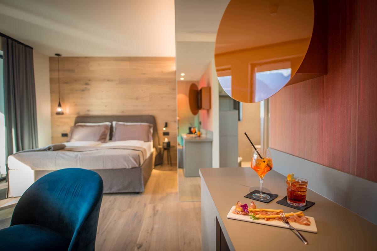 Una habitación de hotel moderna con una pared de madera, una cama, un escritorio con una bebida y un plato de comida, y una silla azul.