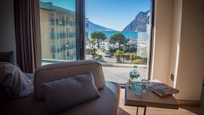 A modern hotel room with a large window offering a view of a coastal town and mountains. - Hotel Villa Enrica (Riva del Garda)