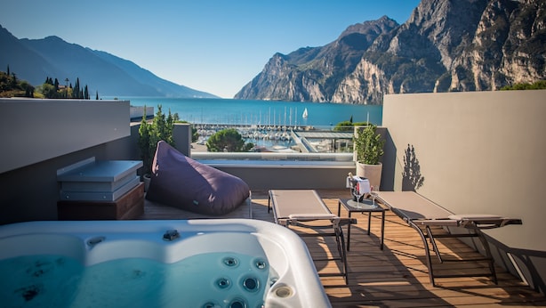 A rooftop terrace with a hot tub, lounge chairs, and a view of a marina and mountains. - Hotel Villa Enrica (Riva del Garda)