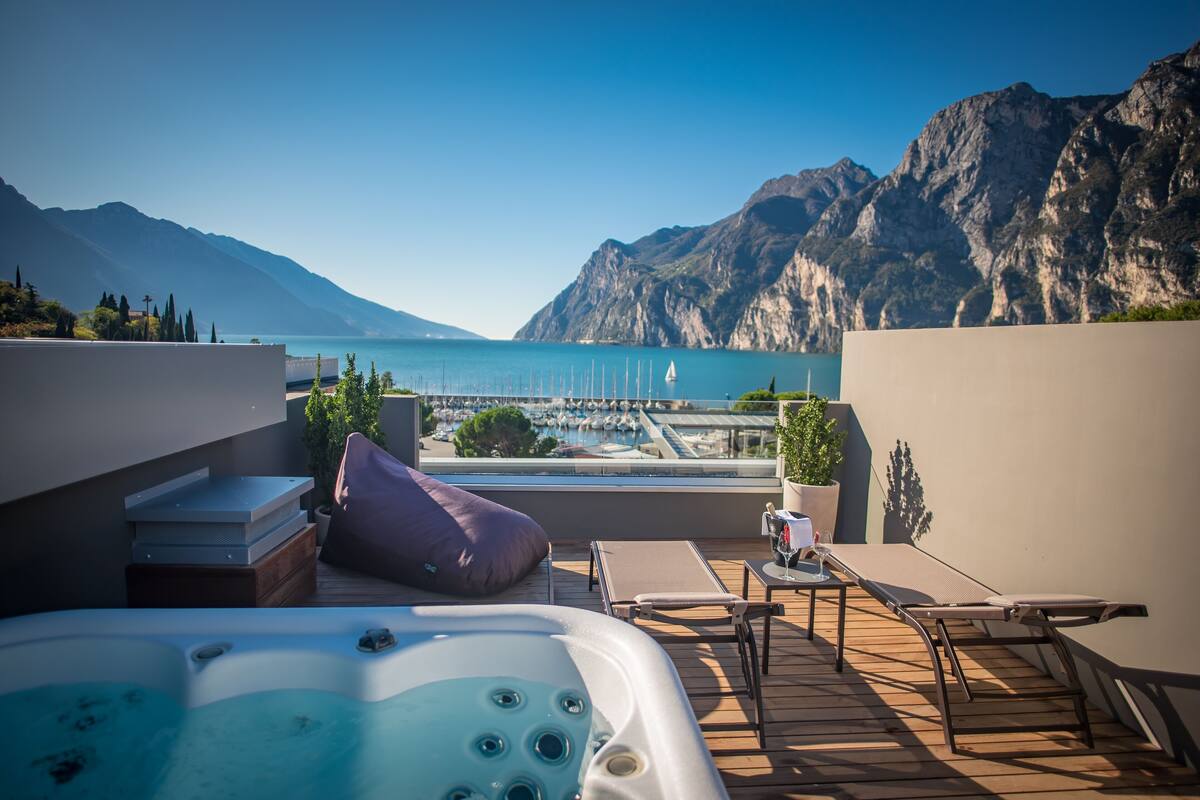 Una terraza en la azotea con un jacuzzi, sillas de descanso y vistas a un puerto deportivo y montañas.