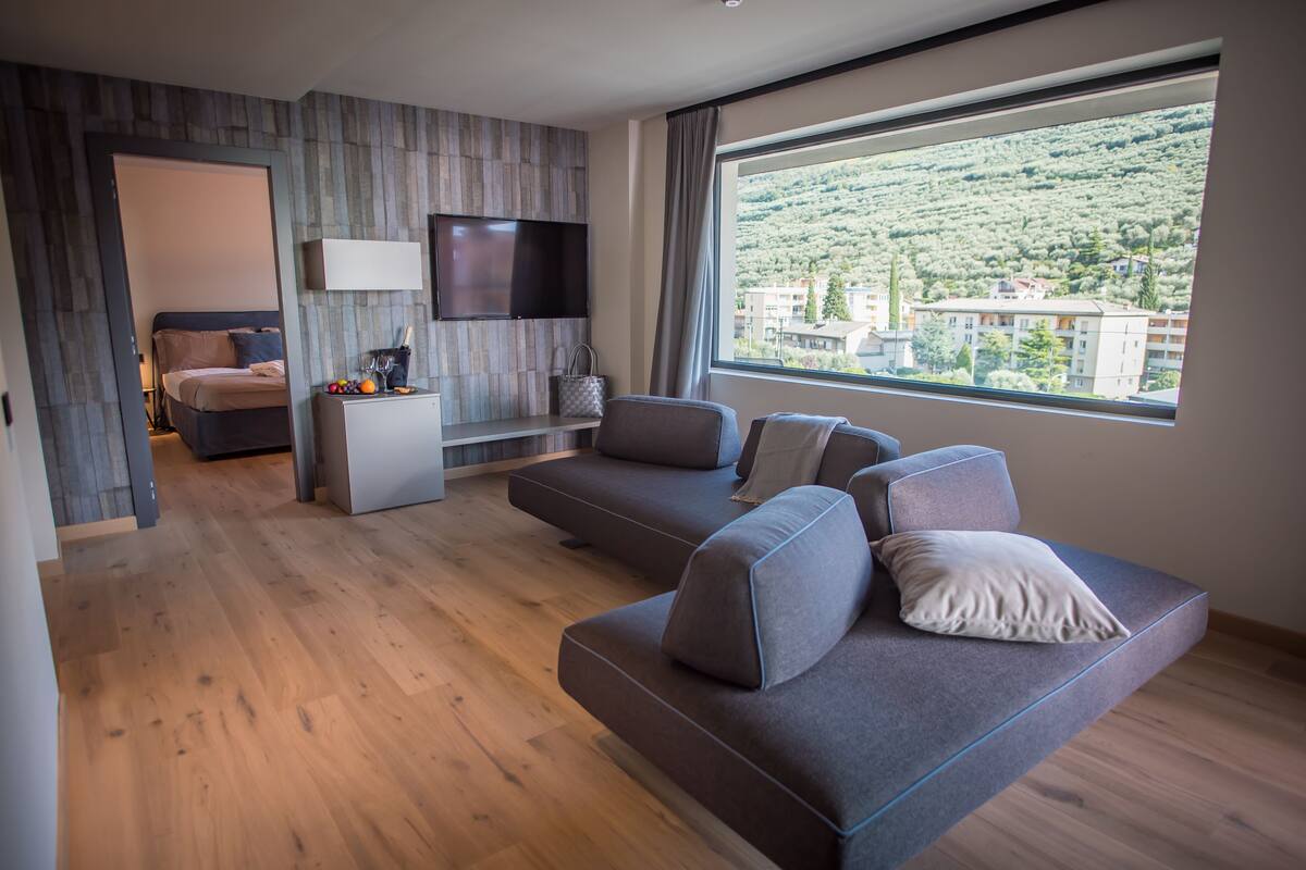 Un salón moderno con un sofá, un televisor montado en la pared y un amplio ventanal con vistas a una colina.