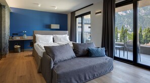 A modern bedroom with a bed, a sofa, a desk, and a large window with a mountain view. - Hotel Villa Enrica (Riva del Garda)