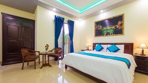 A hotel room with a large bed, two chairs, a small table, a nightstand, and a painting on the wall. - Hoi An Hao Anh Villa (Da Nang)