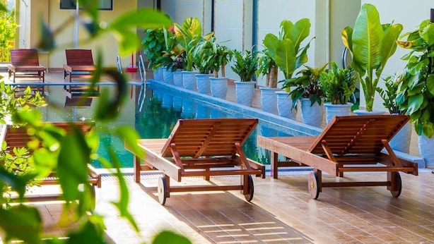 A poolside area with lounge chairs, potted plants, and a building with balconies. - Hoi An Hao Anh Villa (Da Nang)