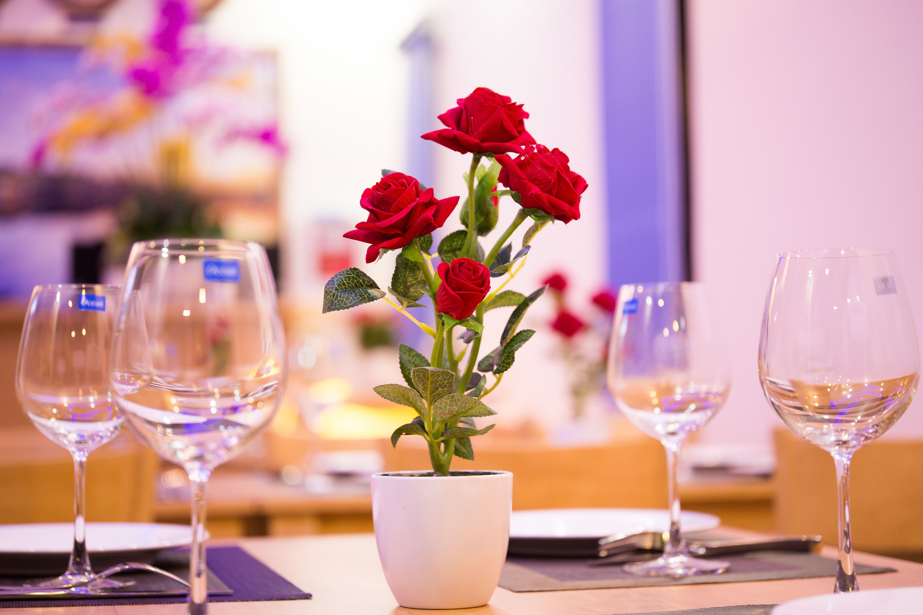 A table with a white vase containing red roses and three empty wine glasses.