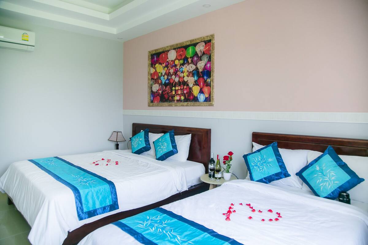 Ein Hotelzimmer mit zwei Betten, jeweils mit blau-weißer Bettdecke, einer Wand-Klimaanlage und einem Wandbild über den Betten.
