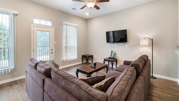 A living room with a brown sectional sofa, a wooden coffee table, a ceiling fan, a flat-screen TV mounted on the wall, and a floor lamp. - Experience a First Class Stay - 2 BDRM (Humble)