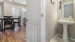 A room with a dining table and chairs, a white door, and a bathroom with a sink and mirror. - Experience a First Class Stay - 2 BDRM (Humble)