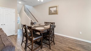 A dining area with a round table, chairs, a chandelier, a staircase, and a framed picture on the wall. - Experience a First Class Stay - 2 BDRM (Humble)