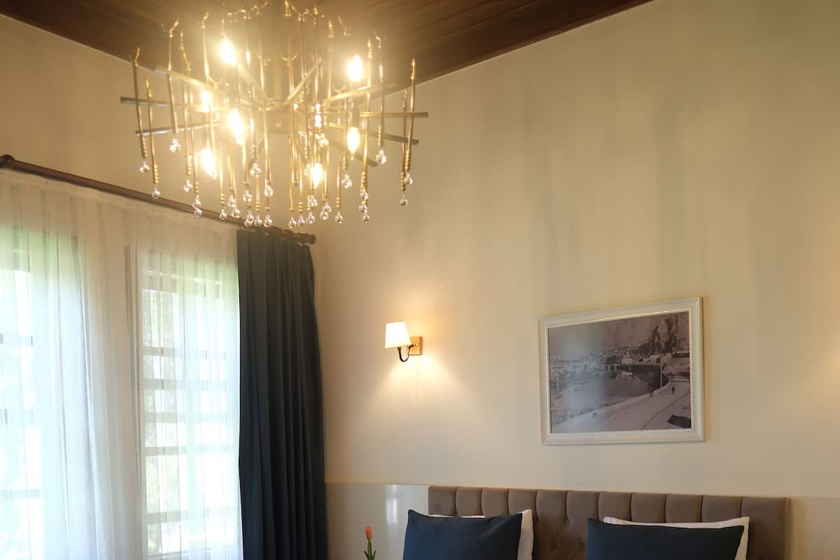 A hotel room with a large bed, a chandelier, a painting on the wall, and a nightstand with a lamp.