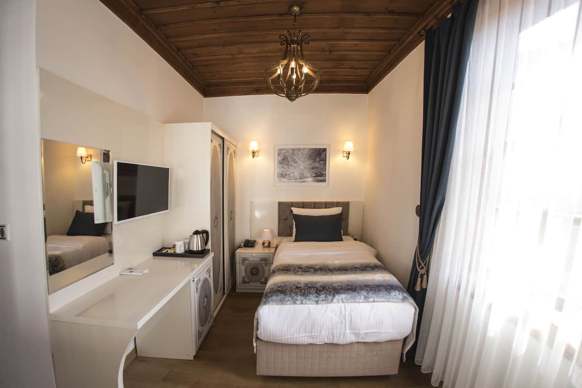 A hotel room with a bed, bedside table, lamp, and a painting on the wall.