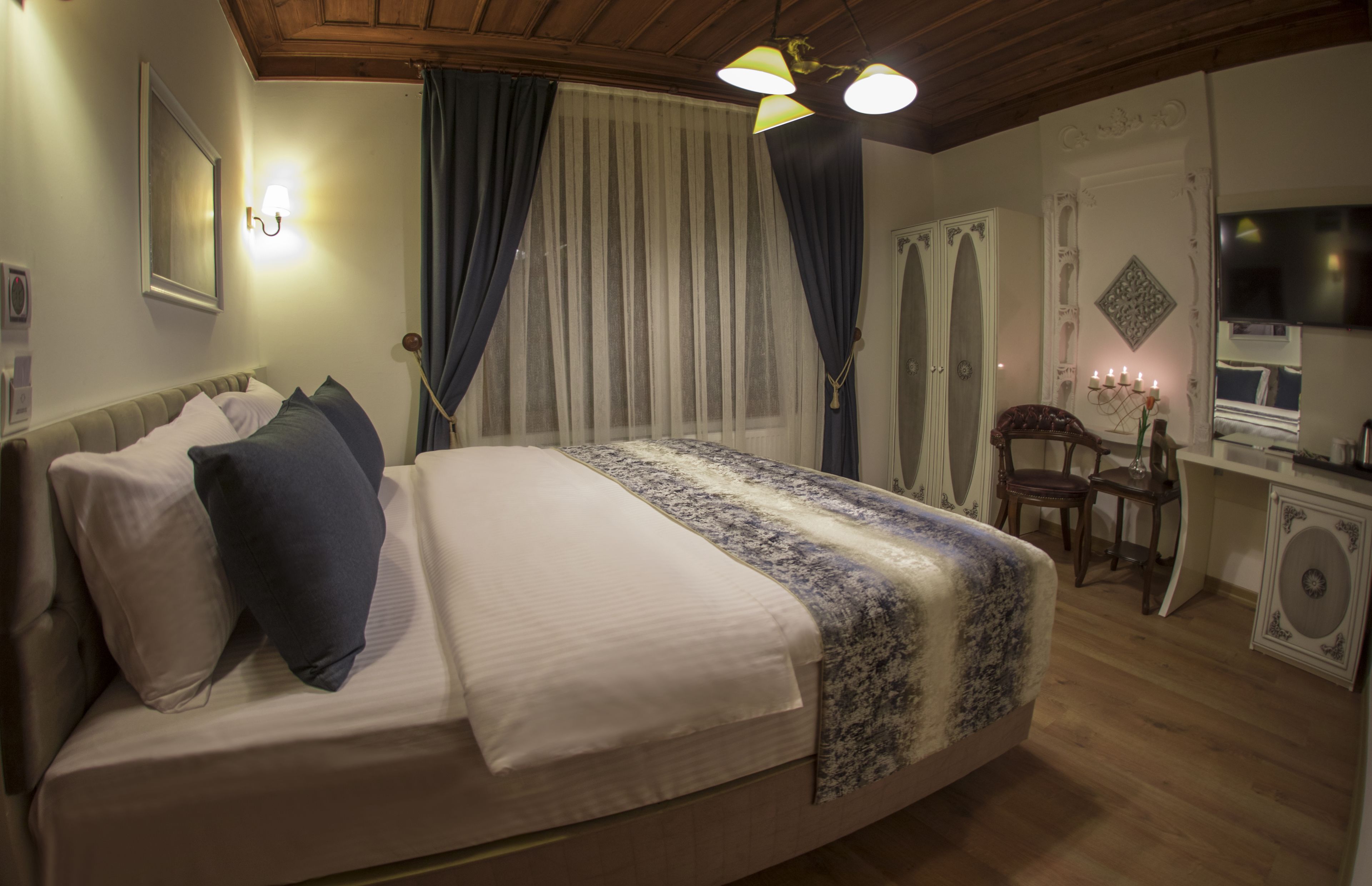 A bedroom with a bed, curtains, a desk with a TV, and a decorative wall piece.