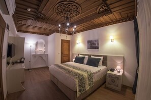 A bedroom with a wooden ceiling, a bed with a green blanket, bedside lamps, and a nightstand with a lamp. - Bayezid Han Konak (Amasya)