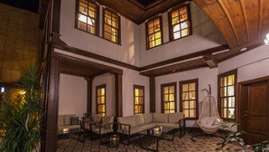 A spacious outdoor seating area with a sofa, chairs, and a hanging chair, surrounded by large windows and a patterned floor. - Bayezid Han Konak (Amasya)