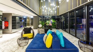 A modern lobby with a blue sofa, yellow and blue cushions, and a glass wall with a view of the street. - The Deck Condominium by Lofty (Patong)