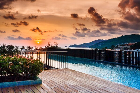 A swimming pool with a wooden deck and a view of the sunset over a hilly landscape.