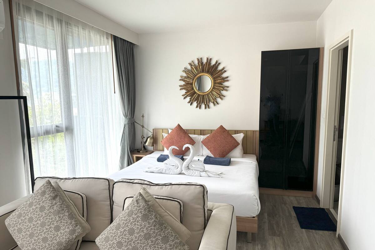 A hotel room with a bed, a sofa, a mirror, and a view of the outdoors.