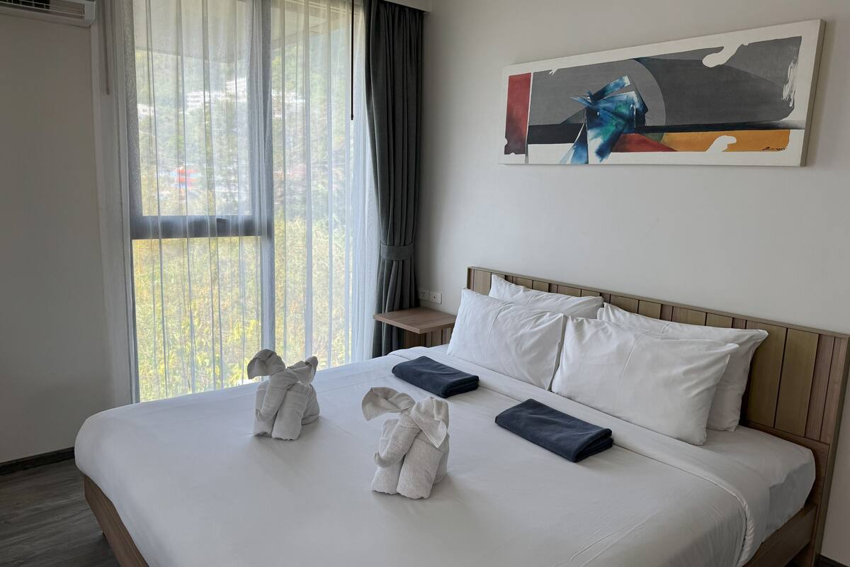 A hotel room with a bed, two towels, a painting, and a window with curtains.