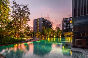 A modern building with a pool, surrounded by trees and greenery.