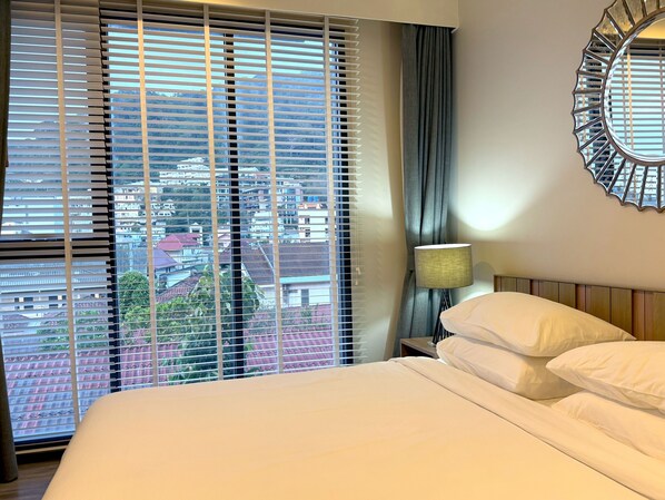 A hotel room with a bed, a nightstand, a lamp, a window with blinds, and a decorative mirror on the wall.