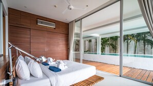 A modern hotel room with a large bed, wooden paneling, a ceiling fan, and a view of a pool and palm trees. - The Quarter by Lofty (Choeng Thale)