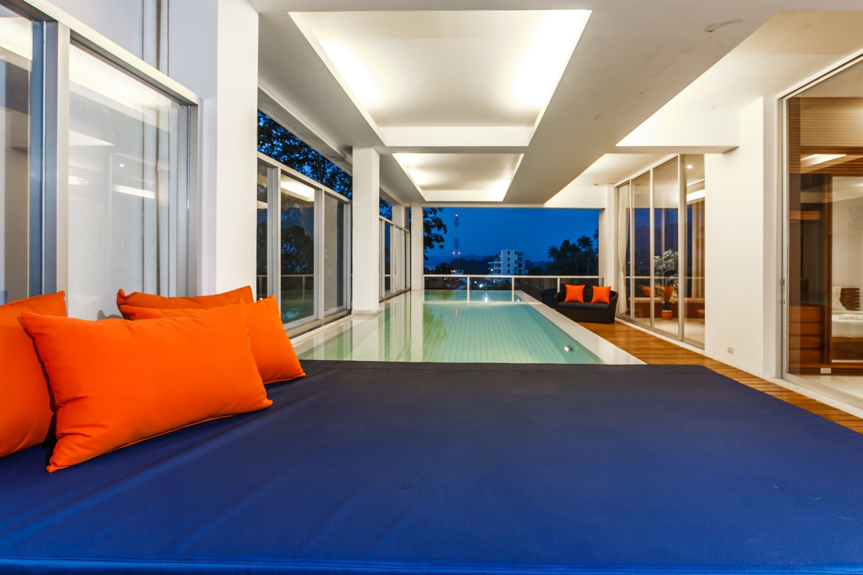 Ein modernes Hotelzimmer mit einem großen Bett, Blick auf den Pool und einem Balkon mit orangenen Kissen.