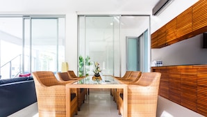A modern dining area with wicker furniture, a glass table, and a view of the outdoors. - The Quarter by Lofty (Choeng Thale)