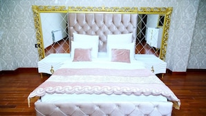 A bedroom with a tufted headboard, two bedside tables, a large mirror, and a patterned bedspread. - Golden Shine Hotel (Baku)